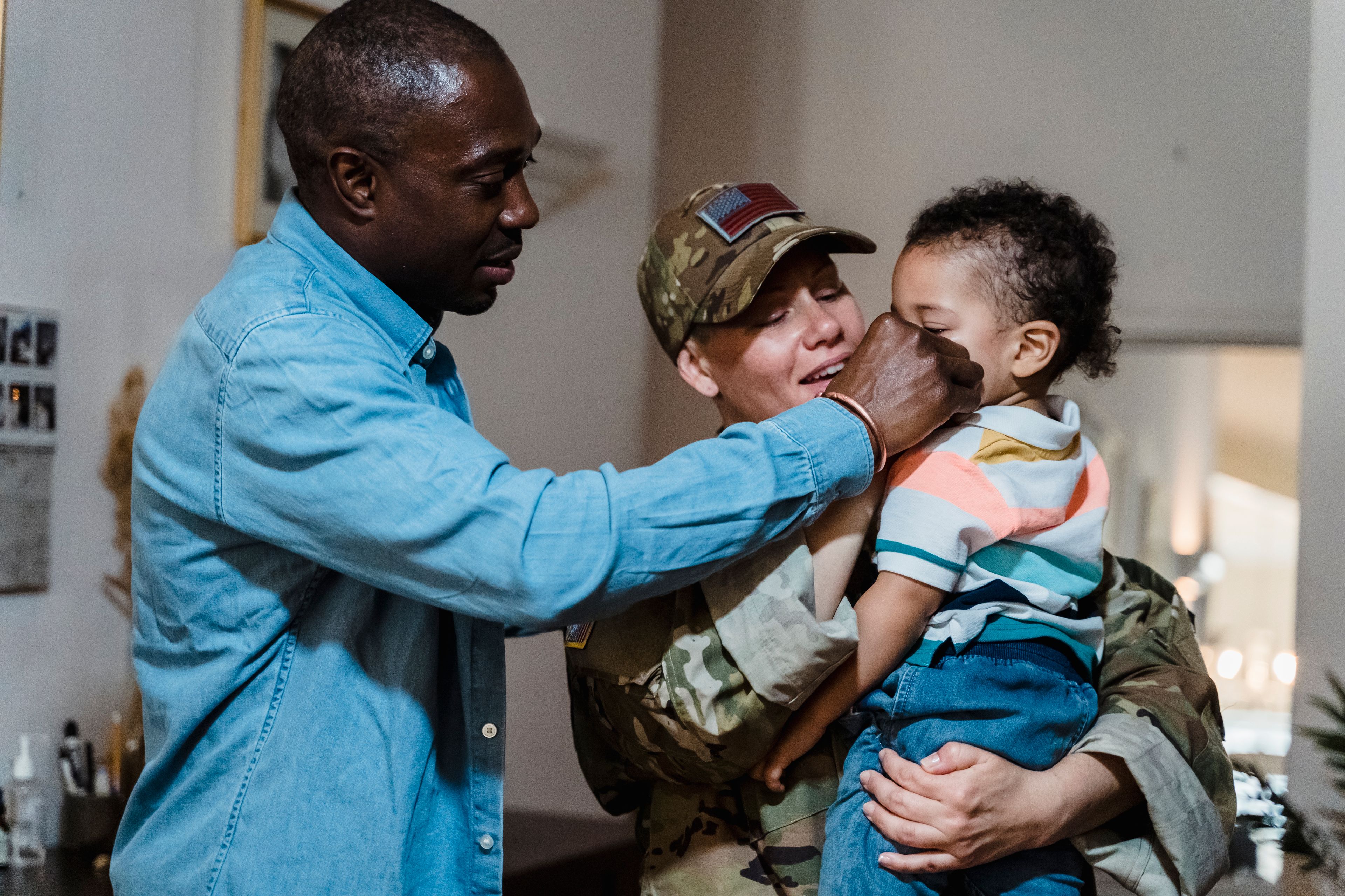 A service member returning home, holding their child as their partner looks on